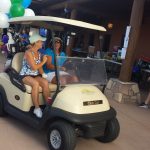 Two people in a golf cart with balloons attached to the back